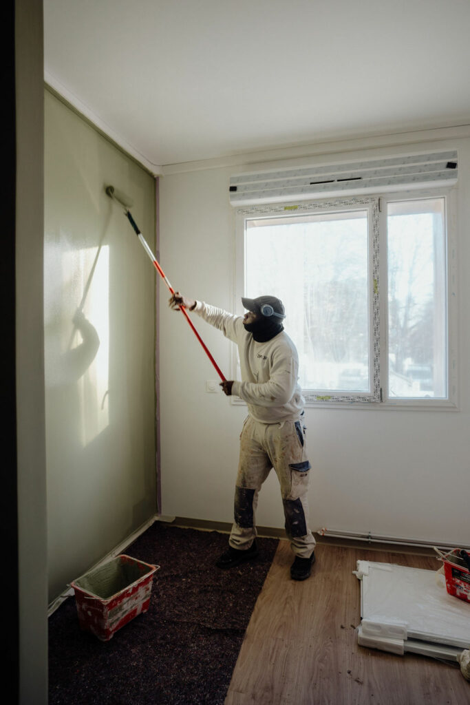 Peintre DPH 34 appliquant la peinture au rouleau sur un mur
